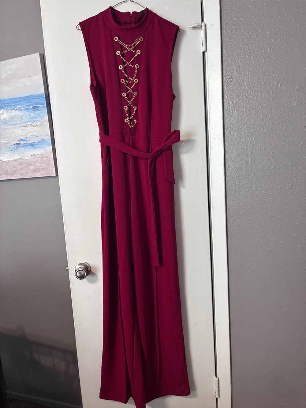 Sleeveless red jumpsuit with gold lace-up detail.